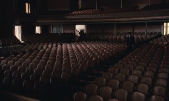 Movie still from “The Bostonians” (1984), directed by James Ivory – An empty theater with rows of seats and a person standing in the middle; Extreme Wide shot, High angle