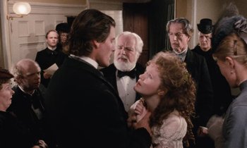 Movie still from “The Bostonians” (1984), directed by James Ivory – A man and a woman in formal wear standing next to each other in front of other people; Medium shot, Over the shoulder angle