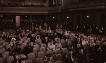 Movie still from “The Bostonians” (1984), directed by James Ivory – A large group of people sitting in a theater; Extreme Wide shot, High angle