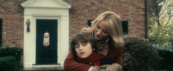 Movie still from “The Box” (2009), directed by Richard Kelly – A woman and a boy are hugging in front of a brick building; Medium shot, Low angle