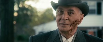 Movie still from “The Box” (2009), directed by Richard Kelly – An older man wearing a suit and a hat; Close Up shot, Over the shoulder angle