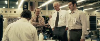 Movie still from “The Box” (2009), directed by Richard Kelly – A group of men standing next to each other in a room; Medium shot, Over the shoulder angle