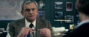 Movie still from “The Box” (2009), directed by Richard Kelly – An older man wearing a suit and tie holding a pencil; Close Up shot, Over the shoulder angle