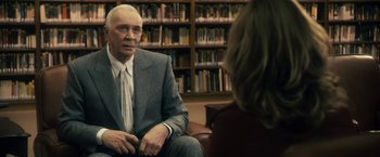 Movie still from “The Box” (2009), directed by Richard Kelly – An older man wearing a suit and tie sitting in front of an older woman; Medium shot, Over the shoulder angle
