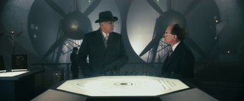 Movie still from “The Box” (2009), directed by Richard Kelly – A man in a suit and hat talking to another man in a suit and hat; Wide shot, Over the shoulder angle