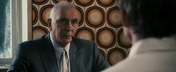 Movie still from “The Box” (2009), directed by Richard Kelly – An older man wearing a suit and tie in front of a wall; Close Up shot, Over the shoulder angle