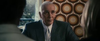 Movie still from “The Box” (2009), directed by Richard Kelly – An older man wearing a suit and tie in front of a window; Close Up shot, Over the shoulder angle