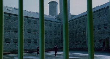 Movie still from “The Boxer” (1997), directed by Jim Sheridan – Two people are walking in a courtyard near a brick building; Extreme Wide shot, High angle