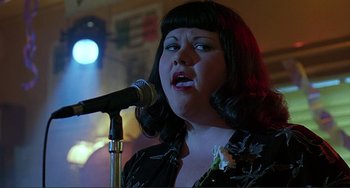 Movie still from “The Boxer” (1997), directed by Jim Sheridan – A woman is singing into a microphone in front of a crowd; Close Up shot, Low angle