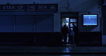 Movie still from “The Boxer” (1997), directed by Jim Sheridan – A group of people standing in front of a building at night; Extreme Wide shot, High angle