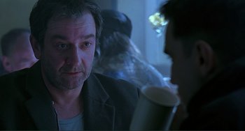 Movie still from “The Boxer” (1997), directed by Jim Sheridan – A man sitting in front of another man holding a drink; Close Up shot, Over the shoulder angle