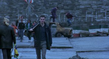 Movie still from “The Boxer” (1997), directed by Jim Sheridan – A man holding a baseball bat while standing on a street; Wide shot, Low angle