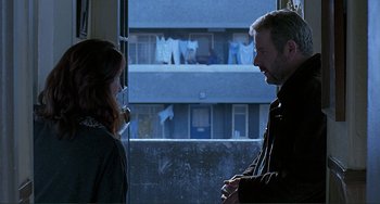 Movie still from “The Boxer” (1997), directed by Jim Sheridan – A man and a woman standing next to each other in front of a building; Medium shot, Over the shoulder angle