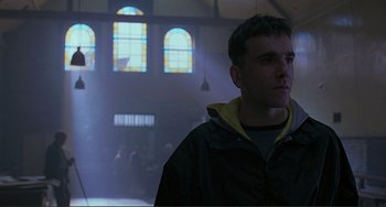 Movie still from “The Boxer” (1997), directed by Jim Sheridan – A man standing in front of stained glass windows in a church; Close Up shot, Low angle