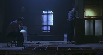 Movie still from “The Boxer” (1997), directed by Jim Sheridan – A man standing next to a table in a dark room; Wide shot, Low angle