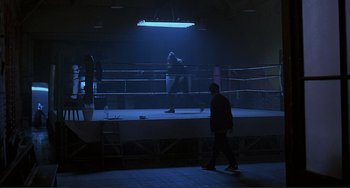 Movie still from “The Boxer” (1997), directed by Jim Sheridan – A man is walking in a boxing ring at night time; Wide shot, High angle