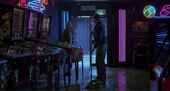 Movie still from “The Boxer” (1997), directed by Jim Sheridan – A man and a woman are standing in front of a row of pinball machines; Wide shot, High angle