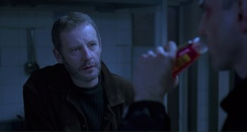 Movie still from “The Boxer” (1997), directed by Jim Sheridan – A man holding a bottle in his hand while looking into the camera; Close Up shot, Over the shoulder angle