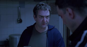 Movie still from “The Boxer” (1997), directed by Jim Sheridan – A man looking at the camera while standing next to another man; Close Up shot, Over the shoulder angle