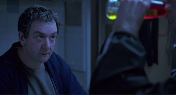 Movie still from “The Boxer” (1997), directed by Jim Sheridan – A man sitting in front of another man in a dark room; Close Up shot, Over the shoulder angle