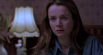 Movie still from “The Boxer” (1997), directed by Jim Sheridan – A woman with long brown hair sitting in front of a lamp; Close Up shot, Over the shoulder angle