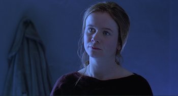 Movie still from “The Boxer” (1997), directed by Jim Sheridan – A young woman in a dark room looking at the camera; Close Up shot, Low angle