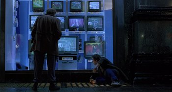 Movie still from “The Boxer” (1997), directed by Jim Sheridan – A man sitting on the ground looking at a television screen; Wide shot, Over the shoulder angle