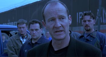 Movie still from “The Boxer” (1997), directed by Jim Sheridan – A person wearing a suit; Close Up shot, Over the shoulder angle