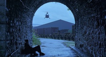 Movie still from “The Boxer” (1997), directed by Jim Sheridan – A person sitting in a tunnel with a helicopter in the background; Extreme Wide shot, Low angle