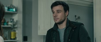 Movie still from “The Boy” (2016), directed by William Brent Bell – A man in a black jacket is standing in a kitchen; Close Up shot, Over the shoulder angle