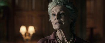 Movie still from “The Boy” (2016), directed by William Brent Bell – An older woman wearing a pearl necklace looking at the camera; Close Up shot, Low angle