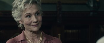 Movie still from “The Boy” (2016), directed by William Brent Bell – An older woman wearing a pink shirt and a pearl necklace; Close Up shot, Over the shoulder angle