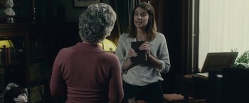Movie still from “The Boy” (2016), directed by William Brent Bell – A woman holding a book talks to another woman in front of a mirror; Medium shot, Over the shoulder angle