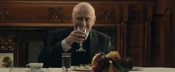 Movie still from “The Boy” (2016), directed by William Brent Bell – An older man sitting at a dinner table drinking wine; Close Up shot, Over the shoulder angle