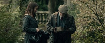 Movie still from “The Boy” (2016), directed by William Brent Bell – An older man and a young woman looking at a package; Medium shot, Over the shoulder angle