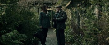 Movie still from “The Boy” (2016), directed by William Brent Bell – A man and a woman standing next to each other on a walkway; Medium shot, Over the shoulder angle