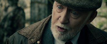 Movie still from “The Boy” (2016), directed by William Brent Bell – An old man with a beard wearing a hat and a tie; Close Up shot, Over the shoulder angle
