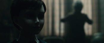 Movie still from “The Boy” (2016), directed by William Brent Bell – A creepy doll is sitting in a dark room; Close Up shot, Over the shoulder angle