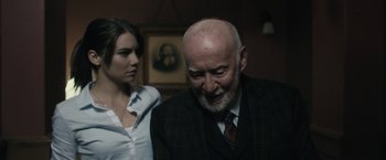 Movie still from “The Boy” (2016), directed by William Brent Bell – An older man and a young woman standing next to each other in a room; Medium shot, Over the shoulder angle