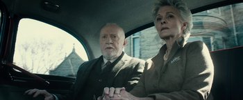 Movie still from “The Boy” (2016), directed by William Brent Bell – An older man and a woman sitting in the back of a car; Medium shot, High angle