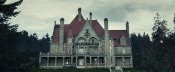 Movie still from “The Boy” (2016), directed by William Brent Bell – An old stone mansion with a large red brick roof; Extreme Wide shot, Low angle