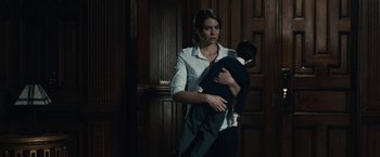 Movie still from “The Boy” (2016), directed by William Brent Bell – A woman holding a baby in her arms in front of a wooden door; Medium shot, Low angle