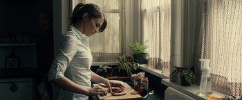 Movie still from “The Boy” (2016), directed by William Brent Bell – A woman cutting a piece of meat on a cutting board; Medium shot, Over the shoulder angle
