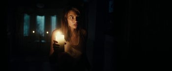 Movie still from “The Boy” (2016), directed by William Brent Bell – A woman holding a lit candle in a dark room; Medium shot, Over the shoulder angle