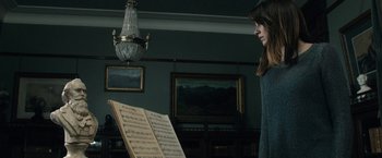Movie still from “The Boy” (2016), directed by William Brent Bell – A woman standing in front of an open sheet music; Medium shot, Over the shoulder angle