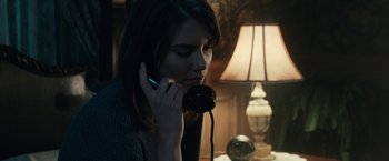 Movie still from “The Boy” (2016), directed by William Brent Bell – A woman is talking on a phone in a dark room; Close Up shot, High angle
