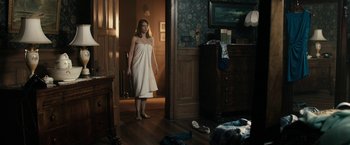 Movie still from “The Boy” (2016), directed by William Brent Bell – A woman standing in a room wearing a towel; Wide shot, Over the shoulder angle