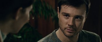 Movie still from “The Boy” (2016), directed by William Brent Bell – A man's face in a room with green plants; Close Up shot, Over the shoulder angle