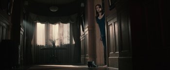 Movie still from “The Boy” (2016), directed by William Brent Bell – A woman leaning against a pillar in a room; Wide shot, Low angle
