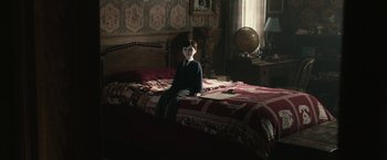 Movie still from “The Boy” (2016), directed by William Brent Bell – A person sitting on a bed in a room; Wide shot, High angle